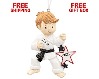 May include: A personalized Christmas ornament of a young martial artist in a white uniform with a black belt. The ornament features the name "Jake" and a star with the year "2025". The figure has light brown hair and is in a karate stance.