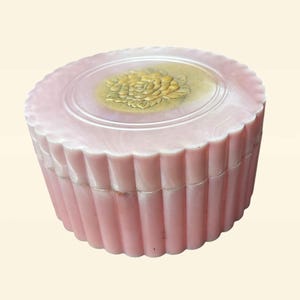 May include: A pink round trinket box with a fluted design and a gold floral design on the lid.