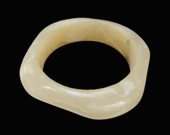 May include: A white, opaque, and slightly textured bangle bracelet. The bracelet is made of a smooth, rounded material and has a slightly irregular shape.