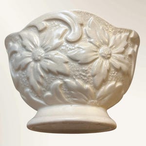 Peut inclure: Bol en céramique blanc cassé avec un socle. Le bol présente un motif floral avec des fleurs et des feuilles en relief et détaillées. Le bord est incurvé et la surface est texturée.