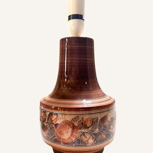 May include: A brown ceramic table lamp with a floral design. The lamp has a white shade and a black cord.