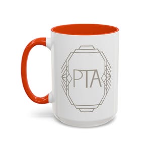 May include: White ceramic mug with an orange interior and handle. The mug features the letters "PTA" inside a geometric design in gray. A simple and stylish design for everyday use.