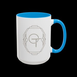 May include: White ceramic mug with a blue interior and handle. The mug features a gray geometric design with the letters "GT" inside. The mug is designed for hot or cold beverages.