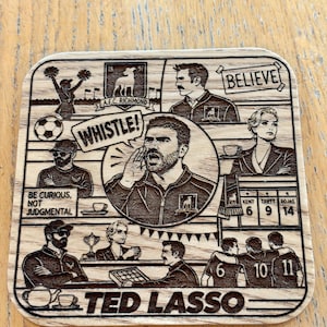 May include: A square wooden coaster featuring laser-engraved illustrations of characters and scenes from the television show Ted Lasso. The design includes the text BELIEVE, WHISTLE, BE CURIOUS, NOT JUDGMENTAL, and TED LASSO, alongside various football-themed icons.