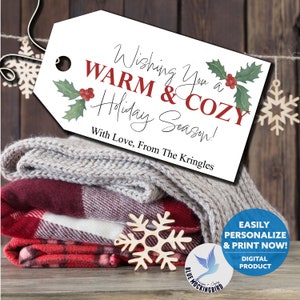 May include: A stack of folded blankets in red plaid, burgundy, and gray, with a wooden snowflake and a tag that reads "Wishing You a Warm & Cozy Holiday Season!" A digital product.
