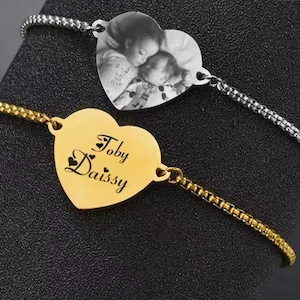 May include: Two gold heart-shaped bracelets. One bracelet features a photo of two children sleeping. The other bracelet has the names "Toby" and "Daissy" engraved on it.