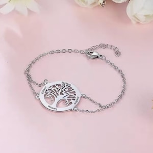 May include: A silver chain bracelet with a tree of life charm. The charm is engraved with the names "Tamine", "Edison", "Jackson", and "Nadine".