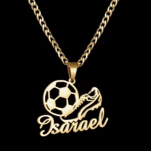 Puede incluir: Collar dorado con un colgante de balón de fútbol y bota de fútbol, con el nombre "Isarael" en escritura cursiva. La cadena es de tipo curb, sobre un fondo negro.