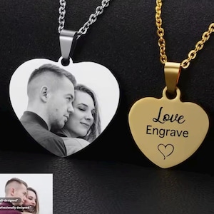 Pode incluir: Dois pingentes em forma de coração de prata e ouro em correntes. Um pingente tem uma foto em preto e branco de um casal, o outro pingente tem as palavras "Love Engrave" com um pequeno símbolo de coração.