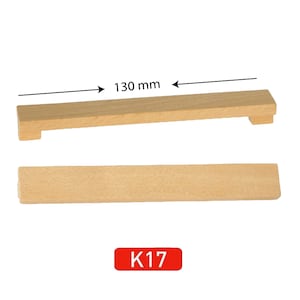May include: A wooden cabinet door pull with a rectangular shape and a 130 mm length. The pull is made of natural wood and has a simple, minimalist design. The pull is labelled "K17".