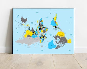 May include: A framed world map print with a light blue background. The continents are colored in shades of gray, yellow, and blue, with black borders. The map is displayed on a light wood floor against a white wall.