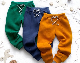 May include: Three pairs of sweatpants in different colors: green, blue, and orange. Each pair has a heart-shaped drawstring.