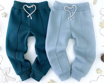 May include: Two pairs of sweatpants, one teal green and one light blue, with a heart-shaped drawstring. Both pairs have a seam down the front of each leg.