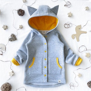 May include: Gray hooded sweatshirt with yellow accents, featuring a button-up front, two pockets, and cat ears on the hood.