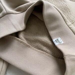May include: A close-up of a beige sweatshirt with a ribbed collar and a small white label that says "smile's world".