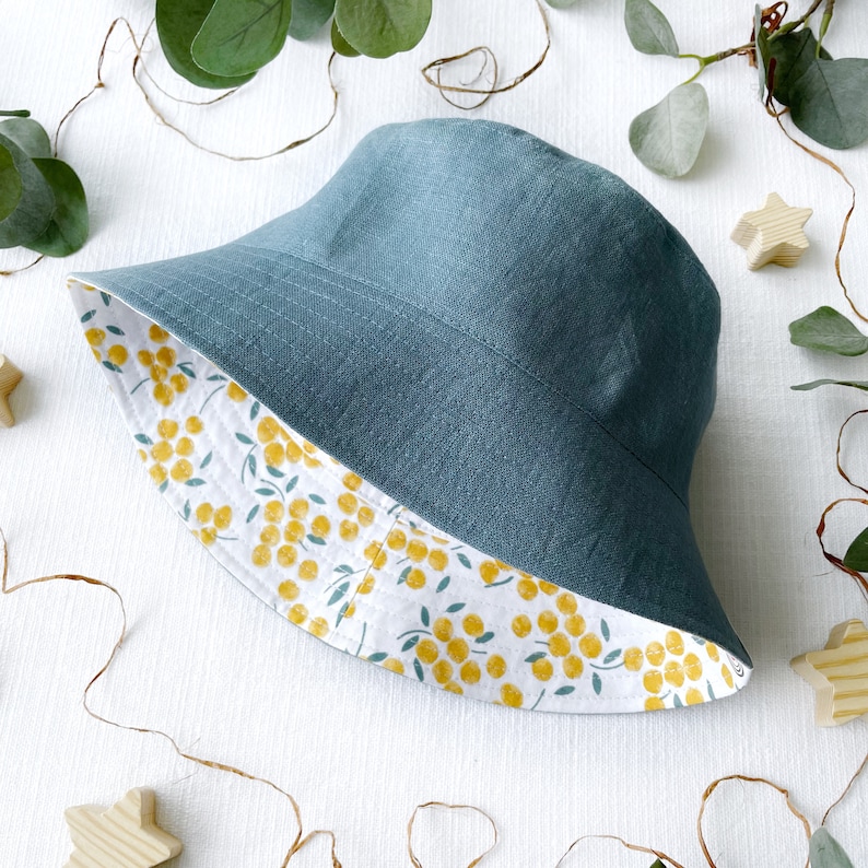 May include: A teal blue bucket hat with a white and yellow floral print lining. The hat is made of a soft, linen fabric.