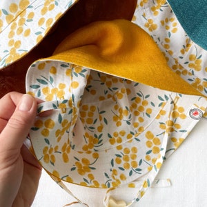 May include: A yellow sun hat with a white and yellow floral print lining. The hat has a tie closure and a small pocket on the inside.