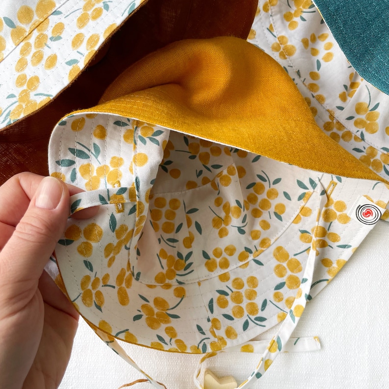 May include: A yellow sun hat with a white and yellow floral print lining. The hat has a tie closure and a small pocket on the inside.