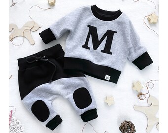 May include: A gray and black baby outfit with a large letter M on the sweatshirt. The pants have black knee patches.