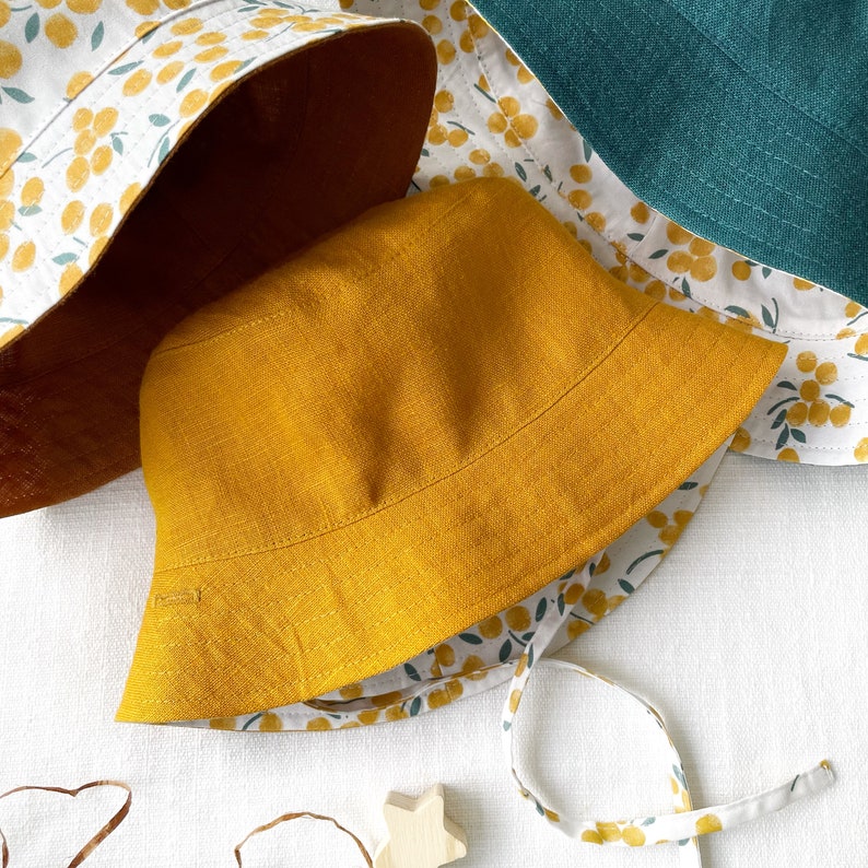 May include: Two sun hats, one with a yellow linen fabric and the other with a white fabric with a yellow floral pattern.