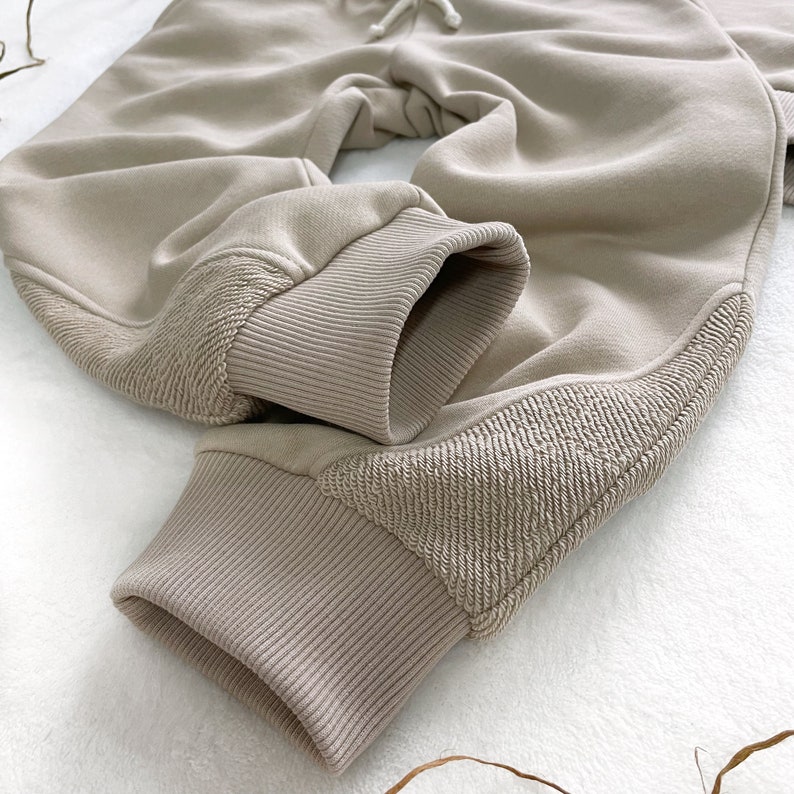 May include: Beige sweatpants with ribbed cuffs and a textured detail on the legs.
