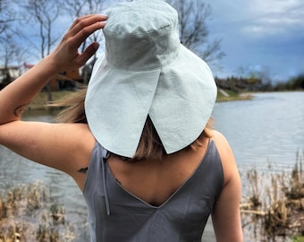 May include: A light blue wide-brimmed sun hat with a pointed crown. The hat is made of a soft, linen-like fabric.