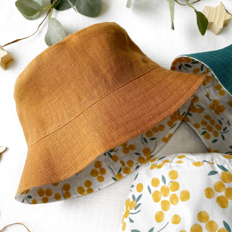 May include: A brown linen bucket hat with a white and yellow floral lining. The hat is reversible and can be worn with either side facing out.