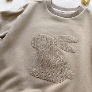 May include: A beige sweatshirt with a large embroidered bunny on the front.