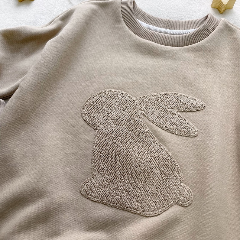May include: A beige sweatshirt with a large embroidered bunny on the front.