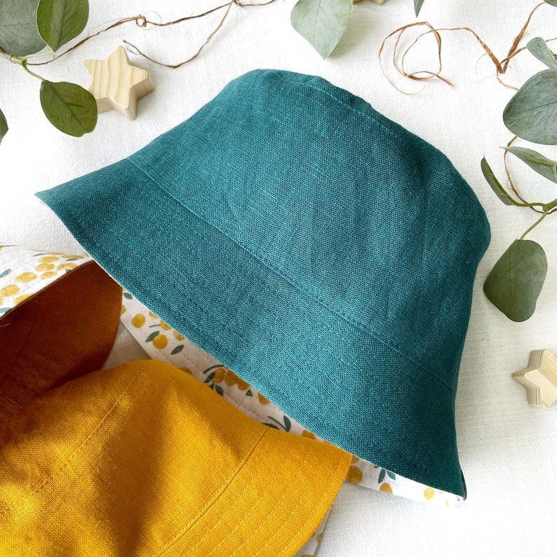 May include: A teal linen bucket hat with a yellow and white floral print lining.