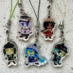 May include: Six clear acrylic charms featuring cartoon characters with various outfits and hairstyles. Each charm has a silver-colored clasp and a colored cord or string. The characters have different skin tones, hair colors, and clothing, including hats and dresses.