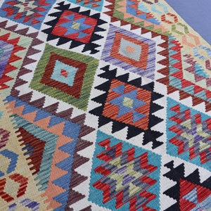 May include: A colorful rug with a geometric pattern in shades of red, blue, green, and white. The rug has a traditional design with intricate details.
