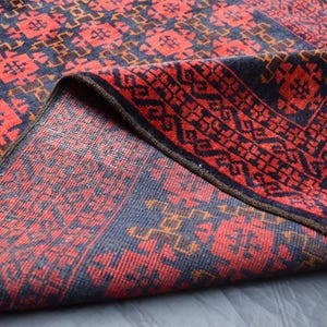 May include: A red and blue patterned rug with a fringe border. The rug is folded in half, showing the intricate design on both sides.