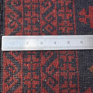 May include: Close-up of a red and black patterned rug with a ruler measuring 8 inches across the rug.