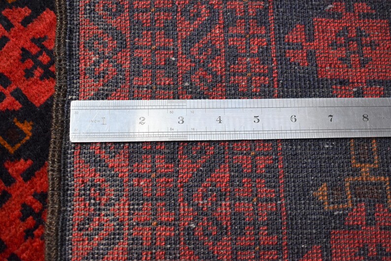 May include: Close-up of a red and black patterned rug with a ruler measuring 8 inches across the rug.
