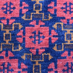 May include: A close-up of a blue and red patterned rug with a geometric design. The rug has a traditional look and is made of woven fibers.