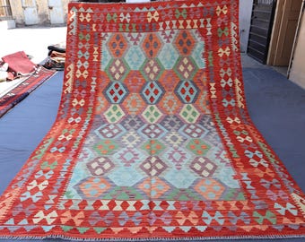May include: A traditional Turkish rug with a red, blue, green, and cream color scheme. The rug features a geometric pattern with intricate details.