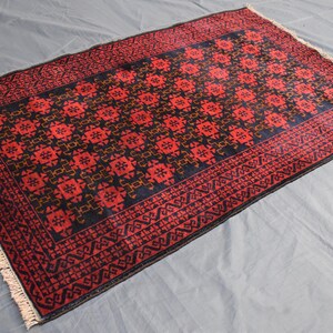 May include: A red and black patterned rug with a geometric design. The rug has a fringe border.