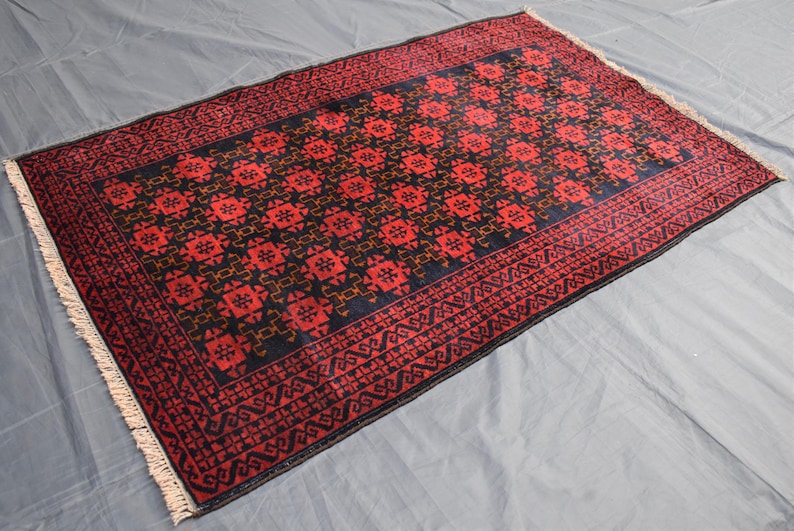 May include: A red and black patterned rug with a geometric design. The rug has a fringe border.