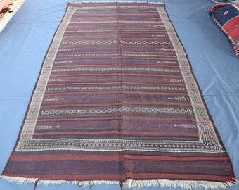 May include: A traditional woven rug with a geometric pattern in shades of red, white, and black. The rug has a fringed edge and is made of natural fibers.