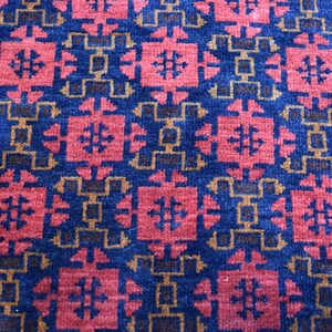 May include: A close-up of a blue and red patterned rug with a geometric design. The rug has a repeating pattern of squares and diamonds.