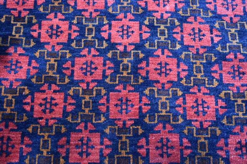 May include: A close-up of a blue and red patterned rug with a geometric design. The rug has a repeating pattern of squares and diamonds.
