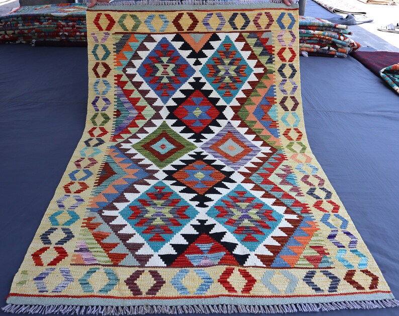 May include: A colorful rug with a geometric pattern in shades of red, blue, green, yellow, and white. The rug has a fringe border and is folded in half.