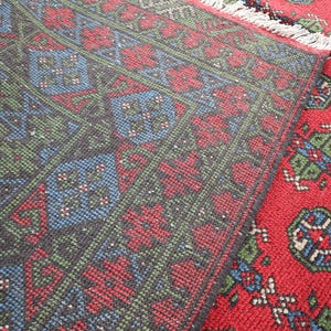 Op de afbeelding: Close-up van een rood, groen en blauw patroonteppich met een franje rand. Het tapijt heeft een traditioneel ontwerp met ingewikkelde details.