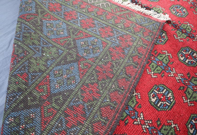 Op de afbeelding: Close-up van een rood, groen en blauw patroonteppich met een franje rand. Het tapijt heeft een traditioneel ontwerp met ingewikkelde details.