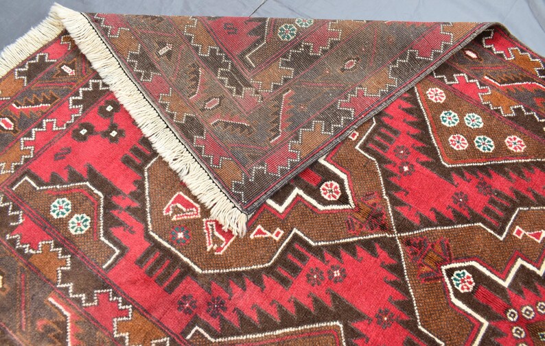 Puede incluir: Una alfombra roja y marr&oacute;n con patrones y flecos en los bordes. La alfombra tiene un dise&ntilde;o geom&eacute;trico con detalles intrincados.