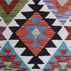 May include: A colorful woven rug with a geometric pattern in shades of red, blue, green, and black. The rug features a central diamond shape with smaller triangles surrounding it.