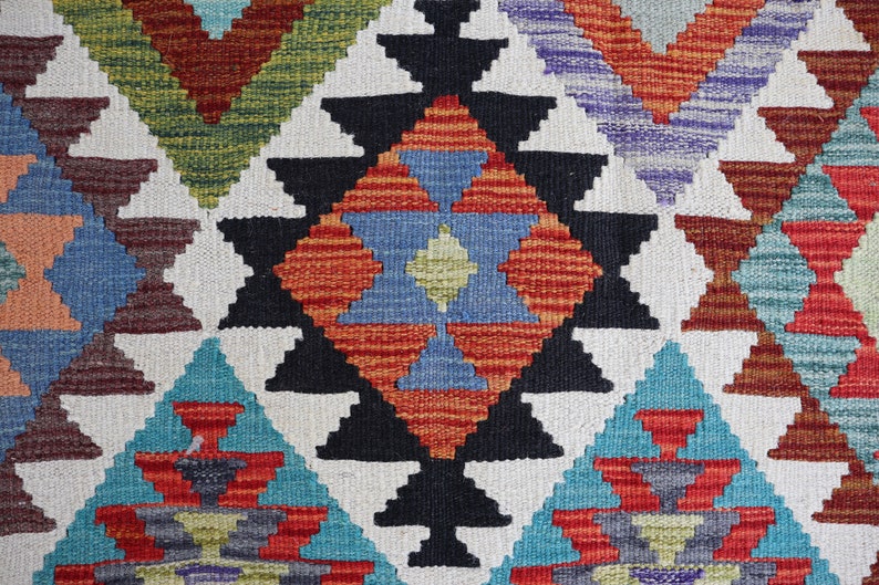 May include: A colorful woven rug with a geometric pattern in shades of red, blue, green, and black. The rug features a central diamond shape with smaller triangles surrounding it.
