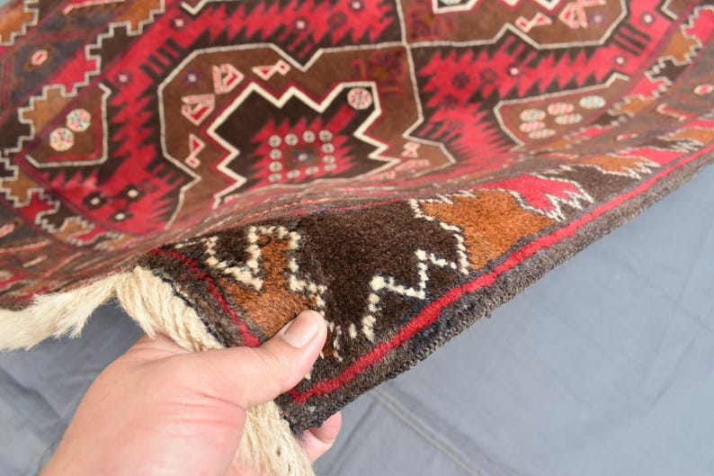 Puede incluir: Primer plano de la parte posterior de una alfombra con estampado rojo, marr&oacute;n y blanco. La alfombra tiene un borde de flecos y est&aacute; hecha de lana.