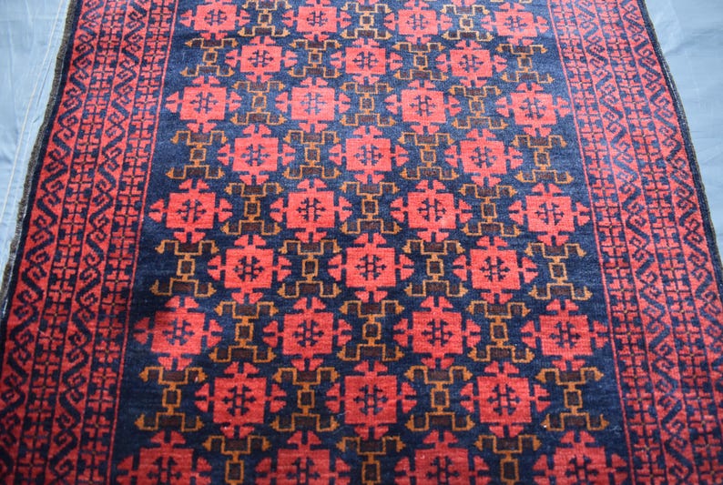 May include: A red, blue, and brown patterned rug with a geometric design. The rug has a border with a repeating pattern.